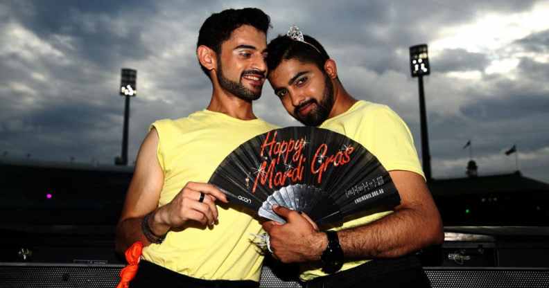Two 2022 Mardi Gras volunteers pose together holding a fan, while wearing lemon yellow t-shirts.