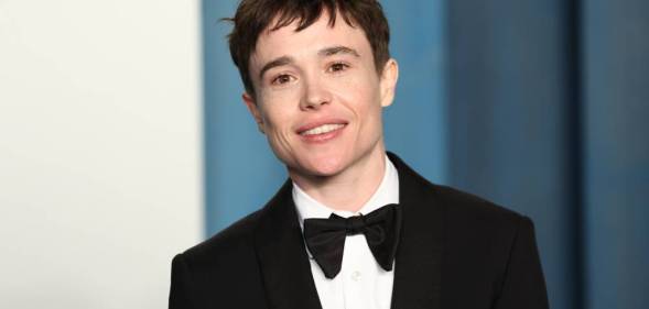 Elliot Page smile at the camera while wearing a white button up shirt, a black bow tie and black suit jacket