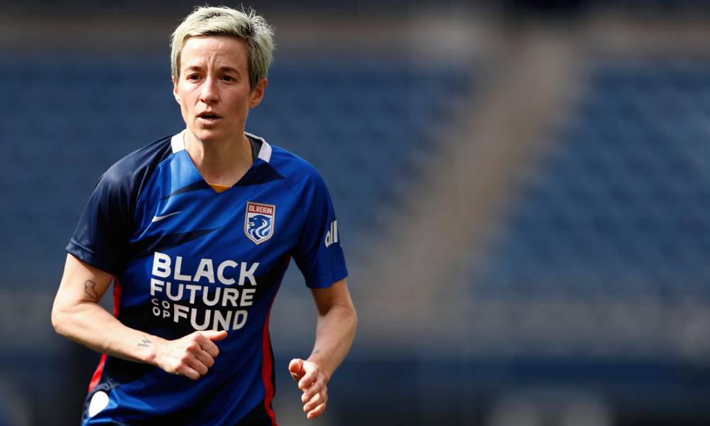 Megan Rapinoe wears a blue OL Reign jersey with the words "Black Future Coop Fund" written in white across her torso as she runs down the field