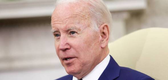 President Joe Biden stares off camera as he speaks to someone. He is wearing a white button up shirt, blue suit jacket and blue tie