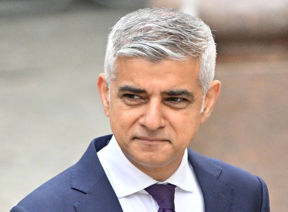 Sadiq Khan stands outside while wearing a white button up shirt, tie and blue suit jacket