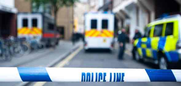 Police officers and vans behind safety police line tape.