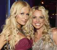 Paris Hilton wears a strapless red dress with a large necklace with her blonde hair down in waves as she stands next to Britney Spears. Spears smiles as she wears a silver, sparkly dress with her blonde hair down in waves