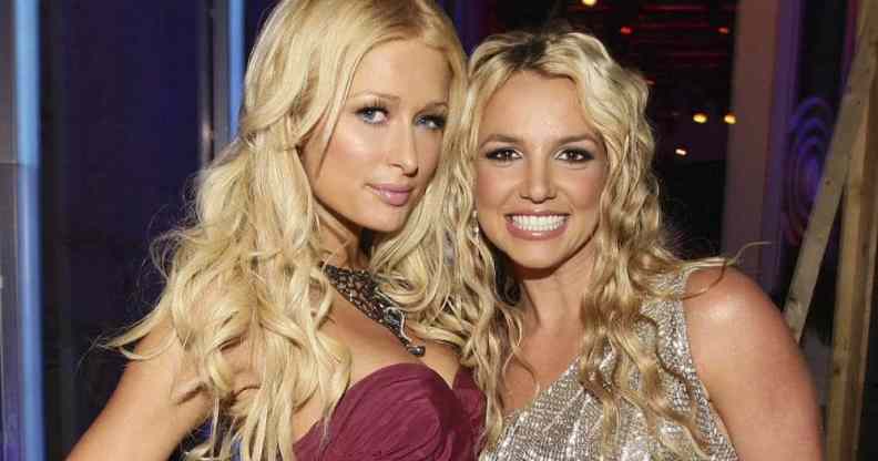 Paris Hilton wears a strapless red dress with a large necklace with her blonde hair down in waves as she stands next to Britney Spears. Spears smiles as she wears a silver, sparkly dress with her blonde hair down in waves
