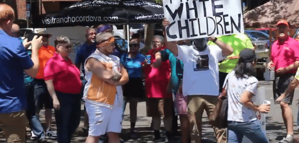 Anti-LGBTQ+ protestors holding a sign that reads 'protect white children'