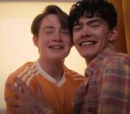 Actors Joe Locke and Kit Connor appear as their characters Charlie and Nick from the LGBTQ+ Netflix series Heartstopper. The characters are smiling while sitting close to each other in a photobooth