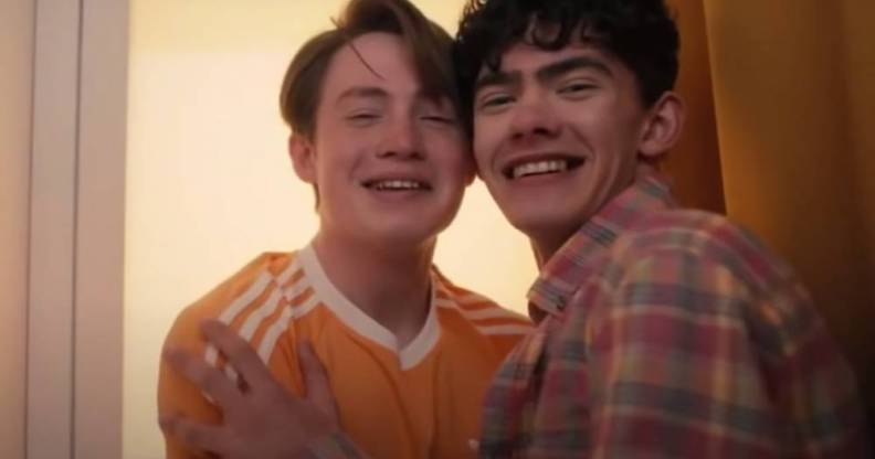 Actors Joe Locke and Kit Connor appear as their characters Charlie and Nick from the LGBTQ+ Netflix series Heartstopper. The characters are smiling while sitting close to each other in a photobooth