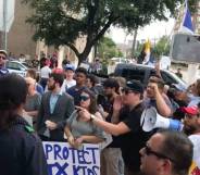 Protestors gather outside a bar in Texas with one person shouting into a megaphone while another person holds a sign reading 'Protect TX kids'