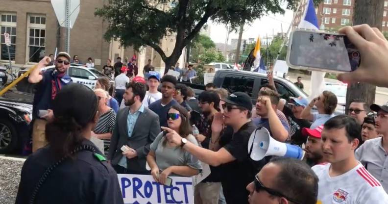 Protestors gather outside a bar in Texas with one person shouting into a megaphone while another person holds a sign reading 'Protect TX kids'