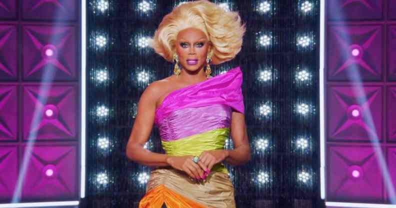 RuPaul wears a one should dress in pink, yellow, tan and orange with a blonde wig on the set of Drag Race All Stars 7