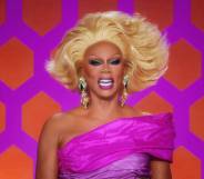 RuPaul laughs while wearing a pink off the shoulder dress, blonde wig and silver sparkly earrings while on the set of Drag Race All Stars 7