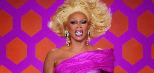RuPaul laughs while wearing a pink off the shoulder dress, blonde wig and silver sparkly earrings while on the set of Drag Race All Stars 7