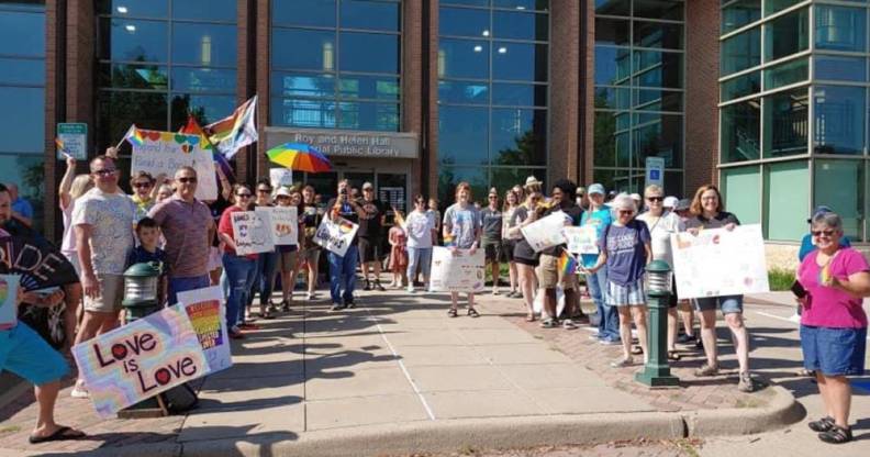 A crowd of people holding up signs in support of the LGBTQ+ community, Pride flags and colourful umbrellas gather outside the Roy and Helen Hall Library in Texas