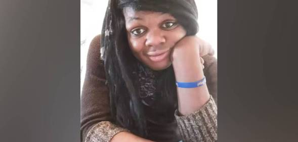 Brazil Johnson, a Black trans woman, wears a brown shirt and blue band on her write as she poses for a picture