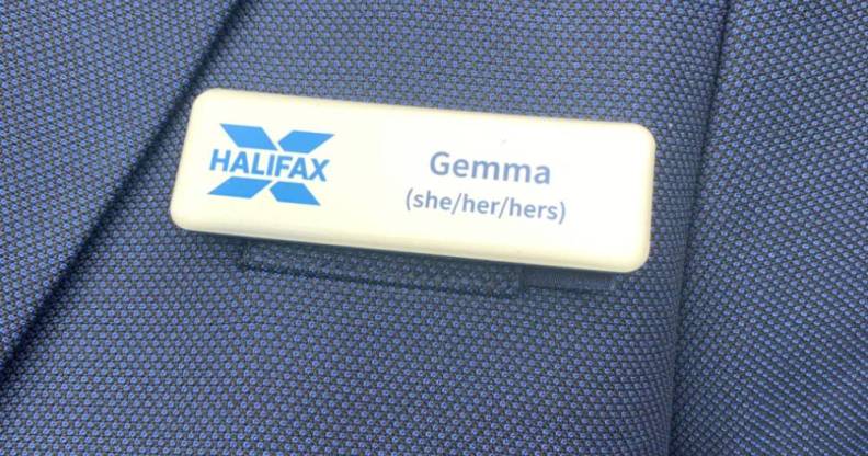 A Halifax employee wears a blue blazer and name badge which includes the name 'Gemma' and her pronouns 'she/her/hers' as well as the blue Halifax logo
