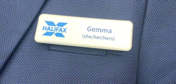 A Halifax employee wears a blue blazer and name badge which includes the name 'Gemma' and her pronouns 'she/her/hers' as well as the blue Halifax logo