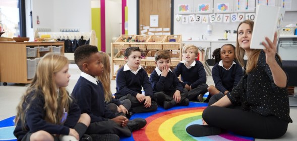 Teacher holding up a book in front of her class of elementary school kids sitting on the floor in a classroom