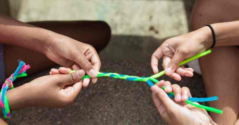 Two people hold fuzzy pipe cleaners which are coloured blue and green which they are braiding together