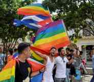 A crowd of people gather in the Prado avenue in Havana, Cuba holding up LGBTQ+ rainbow pride flags as well as the flag of Cuba