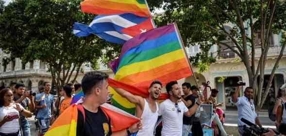 A crowd of people gather in the Prado avenue in Havana, Cuba holding up LGBTQ+ rainbow pride flags as well as the flag of Cuba