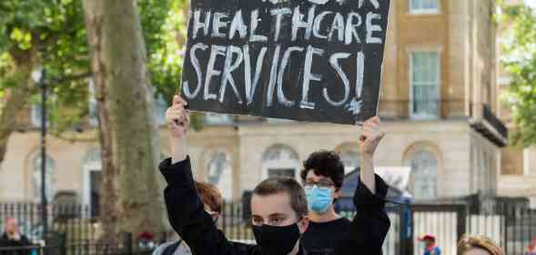 Someone holds up a sign reading: Fund our healthcare services