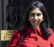Suella Braverman wears a red coat with black buttons as she smiles to camera while standing in front of a black door