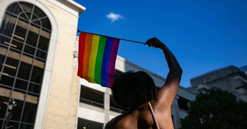 A person waves a rainbow LGBTQ+ Pride flag above their head
