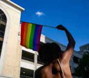 A person waves a rainbow LGBTQ+ Pride flag above their head