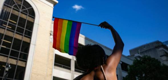 A person waves a rainbow LGBTQ+ Pride flag above their head