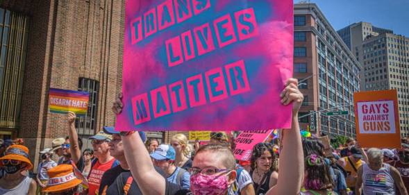 Participant seen holding a pink coloured sign with blue lettering that reads "trans lives matter" at a protest
