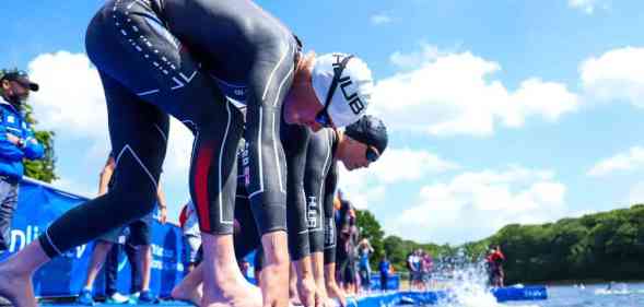 Several people line up on a diving platform as they prepare to dive into a body of water