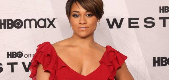 Ariana DeBose wears a red dress with frills on the sleeves as she stands in front of a white background with black logos for HBO Max and Westworld