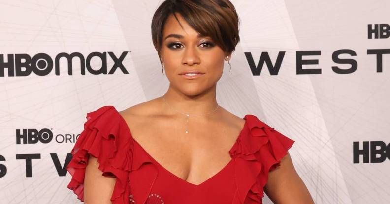 Ariana DeBose wears a red dress with frills on the sleeves as she stands in front of a white background with black logos for HBO Max and Westworld
