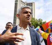 Major of London Sadiq Khan wears a white button up shirt and grey jacket as he attends Pride in London celebrations. A person in the background wears rainbow clothing as they hold up an LGBTQ+ Pride flag