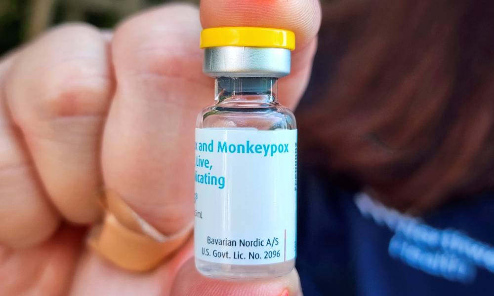 A person holds up a vile of a vaccine with the white label reading monkeypox
