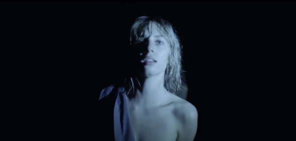 Maya Hawke in "Thérése" music video shirt half on with black backdrop