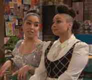 Raven's Home character Nikki (Juliana Joel) wears a white dress with a blue damask pattern on it as she speaks to Raven Baxter (Raven-Symoné). Raven is wearing a white button up shirt, glittery small tie and black and silver patterned vest. Her hair is styled up in three bunches running down her head.