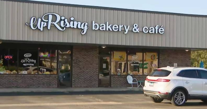 The image shows a business front with the words 'UpRising Bakery and Cafe' written in white. A white car is parked outside in the parking lot