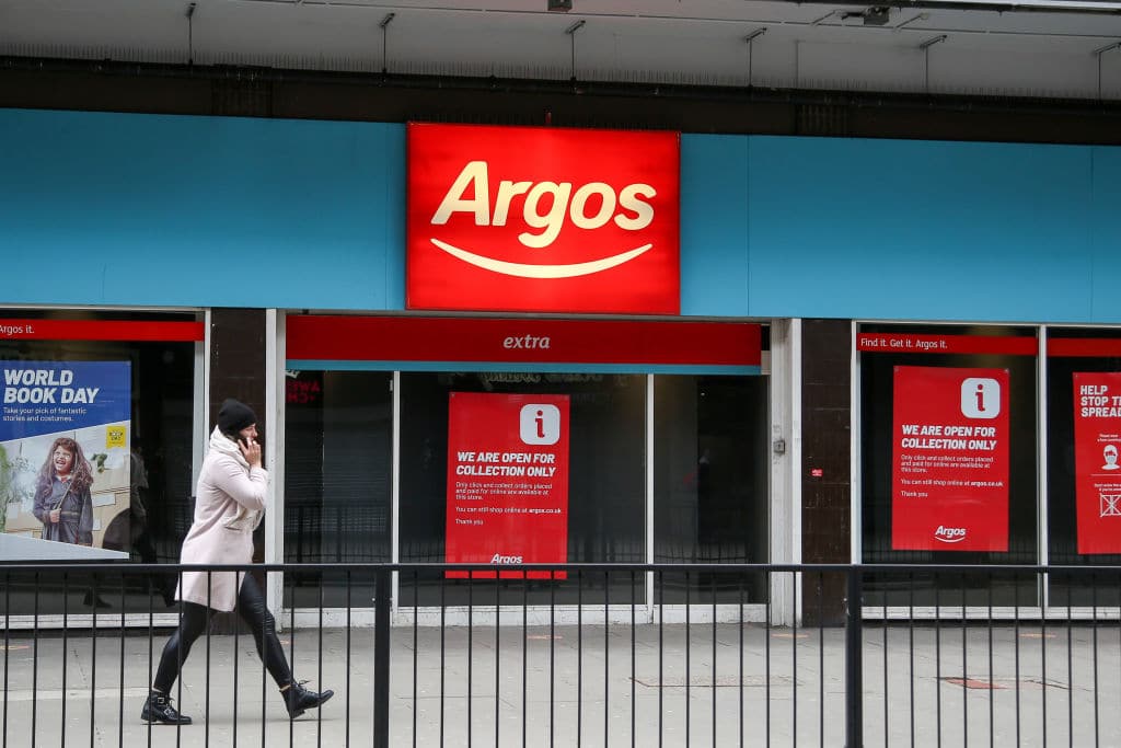 A person communicating on a mobile phone walks past a branch of Argos