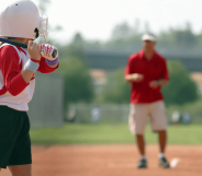 Stock image of a young girl holding a bat while a man coaches her in the background