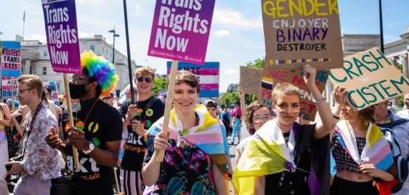 People marching in London Trans+ Pride with placards reading: 'Trans Rights Now' and 'Gender ejoyer binary destroyer'