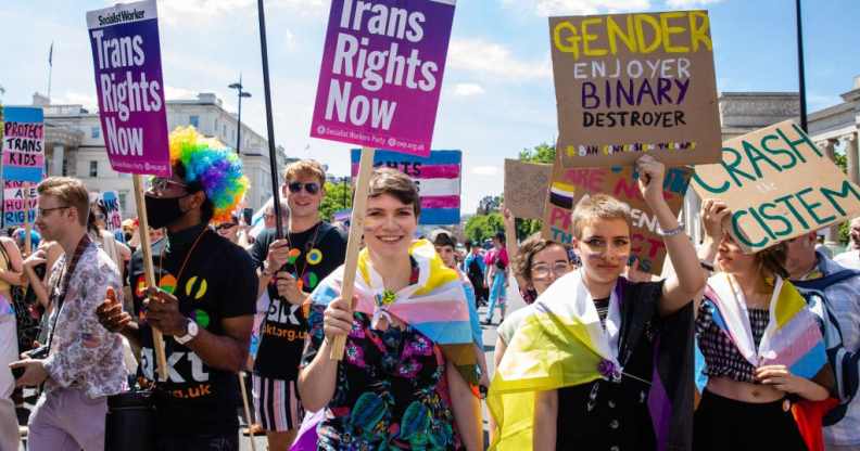 People marching in London Trans+ Pride with placards reading: 'Trans Rights Now' and 'Gender ejoyer binary destroyer'