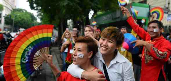 A crowd of people holding rainbow coloured items walk through a LGBTQ+ Pride parade in Vietnam