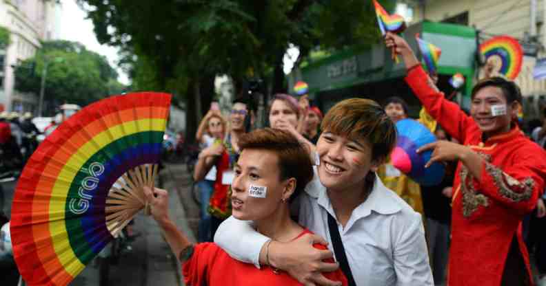 A crowd of people holding rainbow coloured items walk through a LGBTQ+ Pride parade in Vietnam