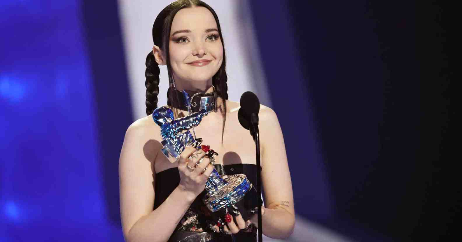 Dove Cameron holds up an MTV VMAs Moon Man award on stage
