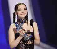 Dove Cameron holds up an MTV VMAs Moon Man award on stage