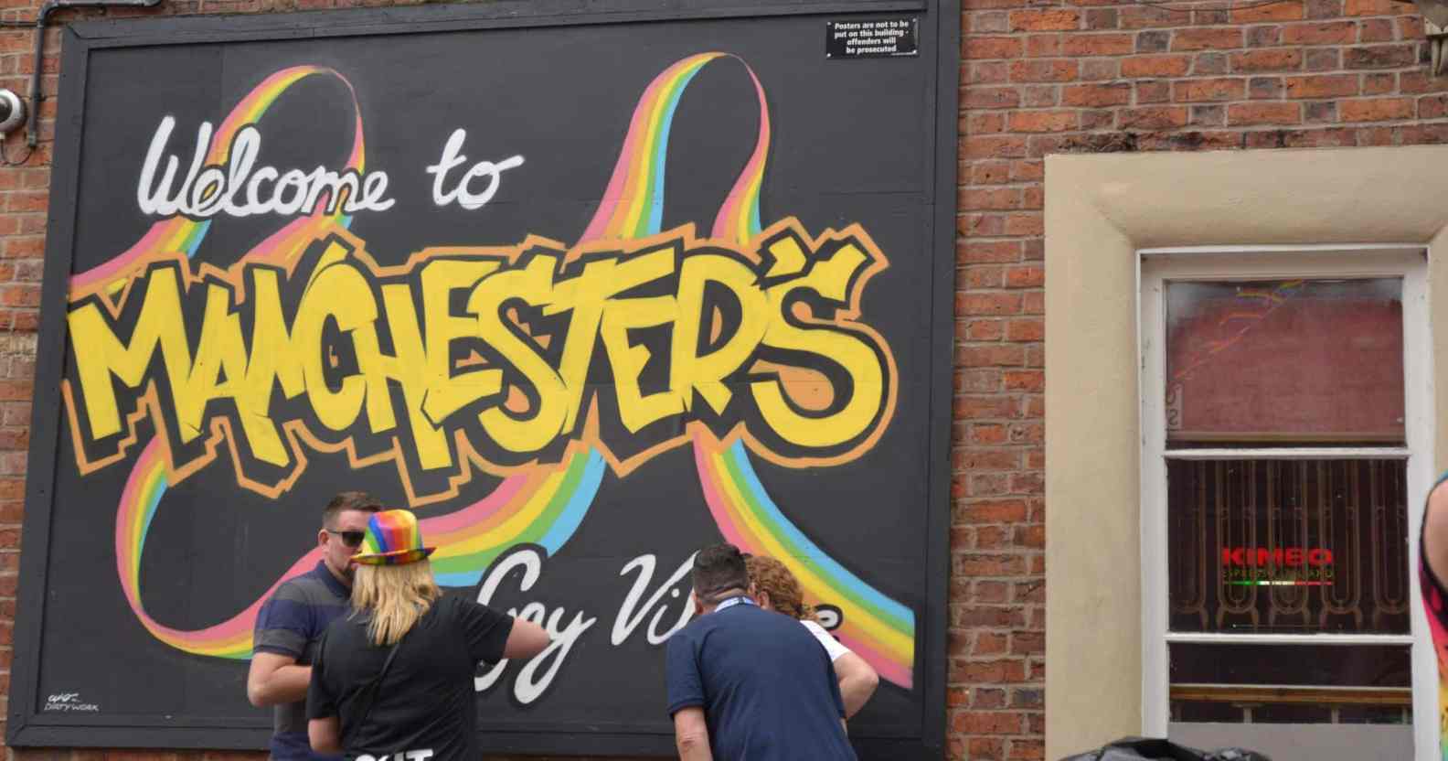 People stand next to a rainbow coloured sign for Manchester's Gay Village