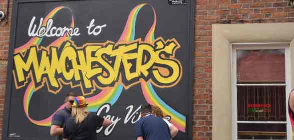 People stand next to a rainbow coloured sign for Manchester's Gay Village