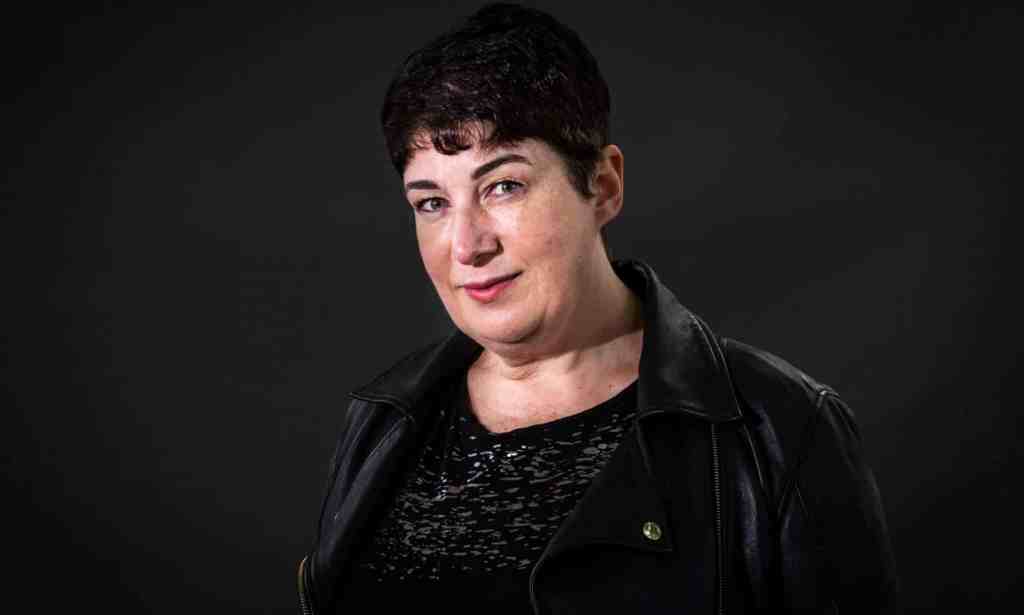 Joanne Harris wears a dark shirt and jacket while standing in front of a dark background