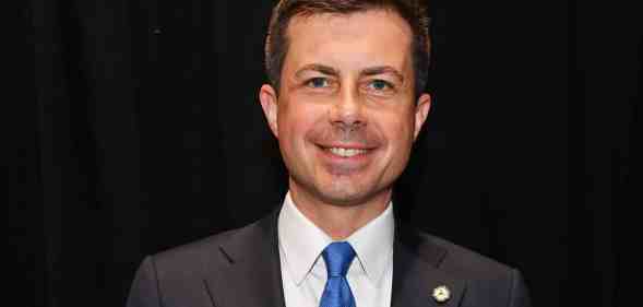 Pete Buttigieg smiles at the camera while wearing a suit and tie